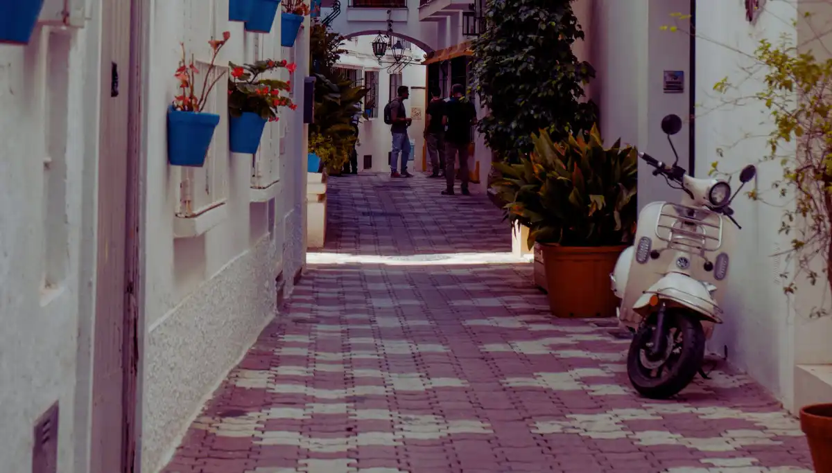 Narrow whitewashed street in Marbella Old Town with blue flower pots and a parked scooter