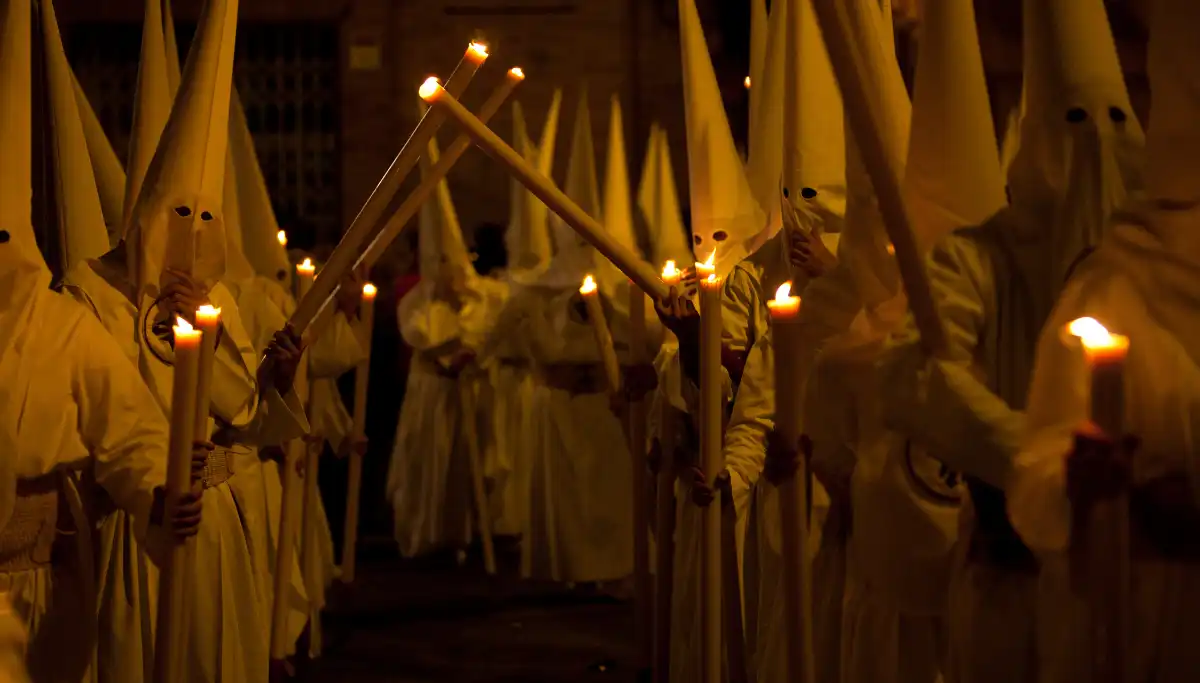 Hooded penitents carrying candles during a Semana Santa procession in Seville at night