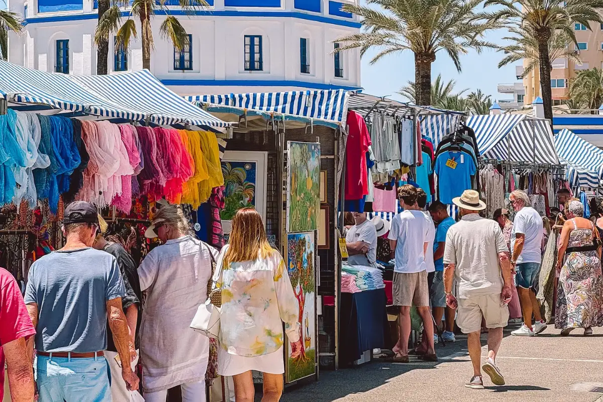 A walkway lined with people looking at craft and clothing booths in Estepona on a suny day.