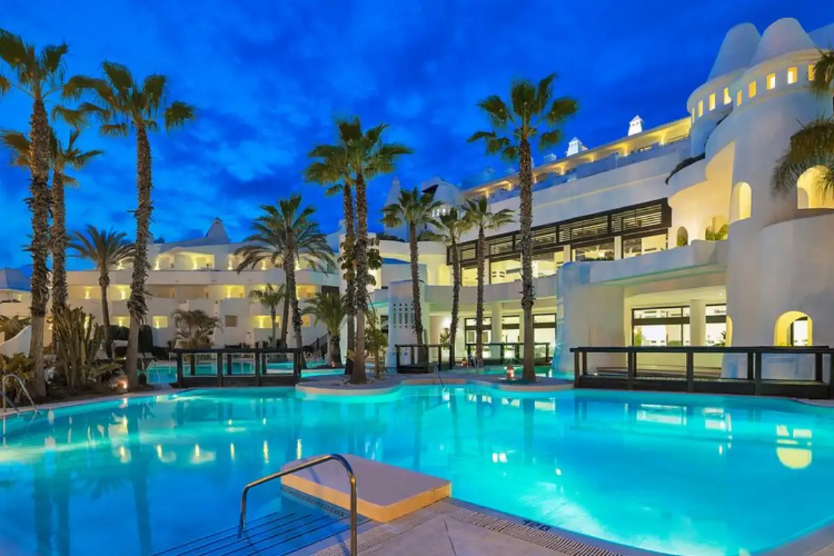 A blue pool with white apartments lining it at night at the H10 Estepona Palace in Estepona.