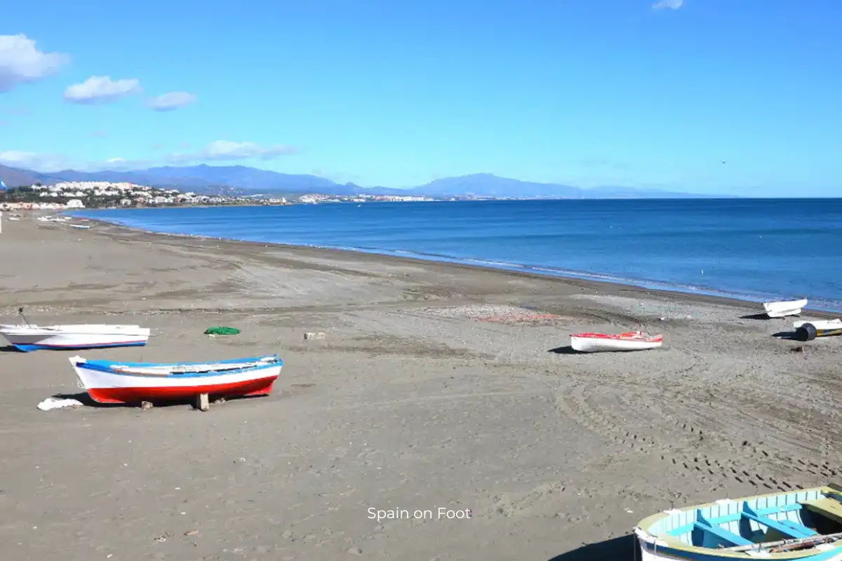 old boats on a deep stretch of brown sand with blue ocean at playa de sabanillas.