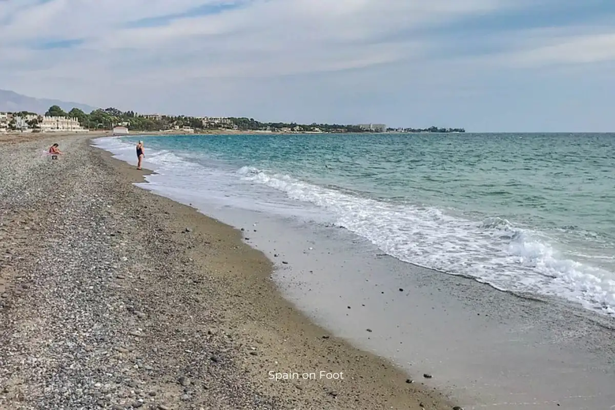 rough sand, choppy ocean water and a stretch of coast with apartments in the background at Playa el Saladillo.