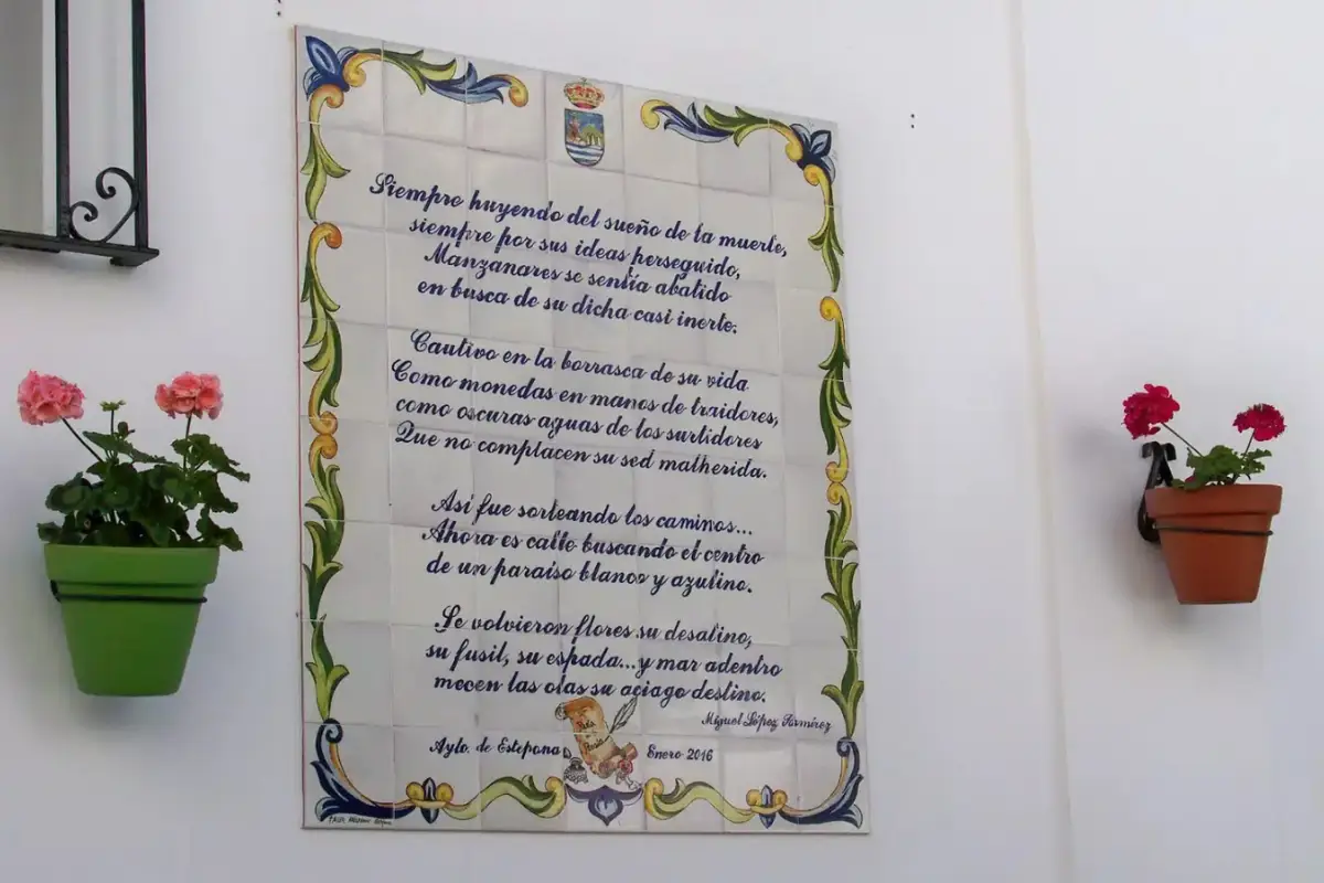 A tile on a wall with flower pots on either side that has poetry written on it in Estepona.