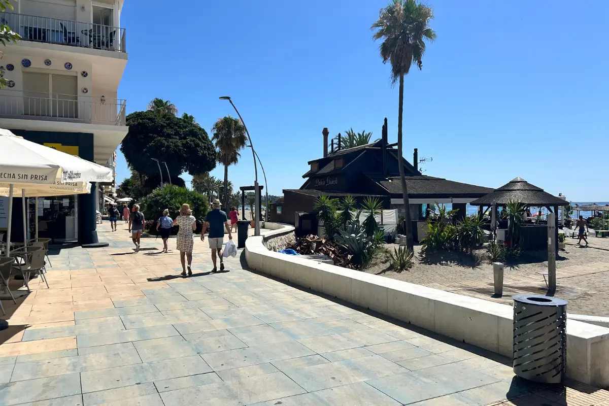 People walking Estepona's Paseo Marítimo with restaurants on one side and beach on the other