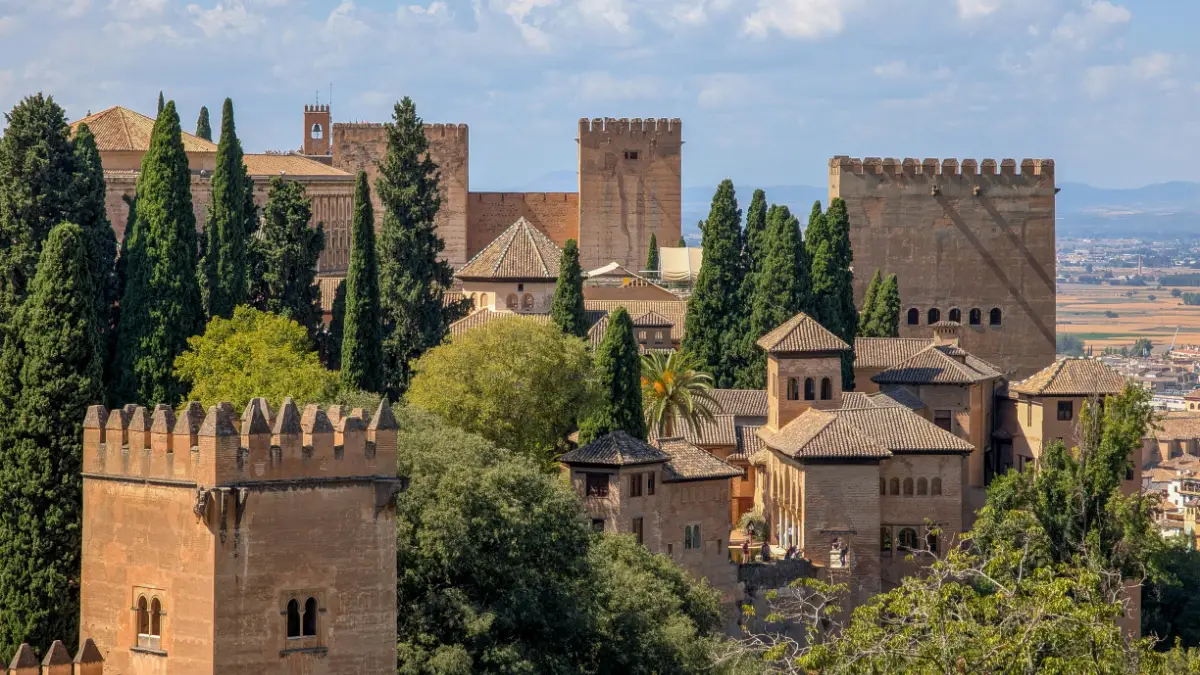 Aerial view of the Alhambra palace towers and rooftops surrounded by cypress trees in Granada