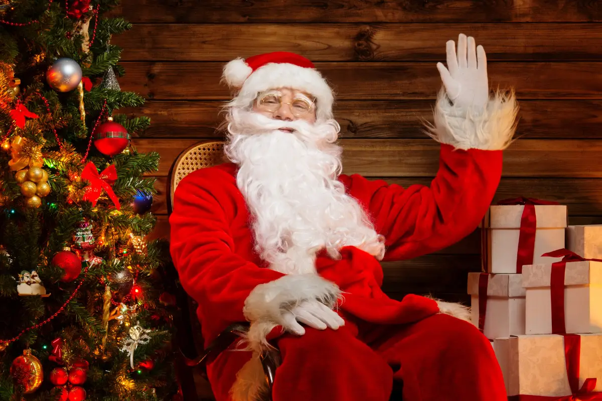 Santa in a red suit and white beard is waving.