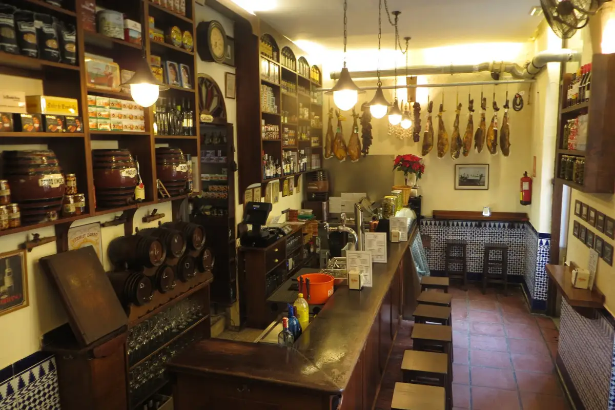 stools in front of a bar with hanging legs of ham at Colmado93 restaurant in Malaga.