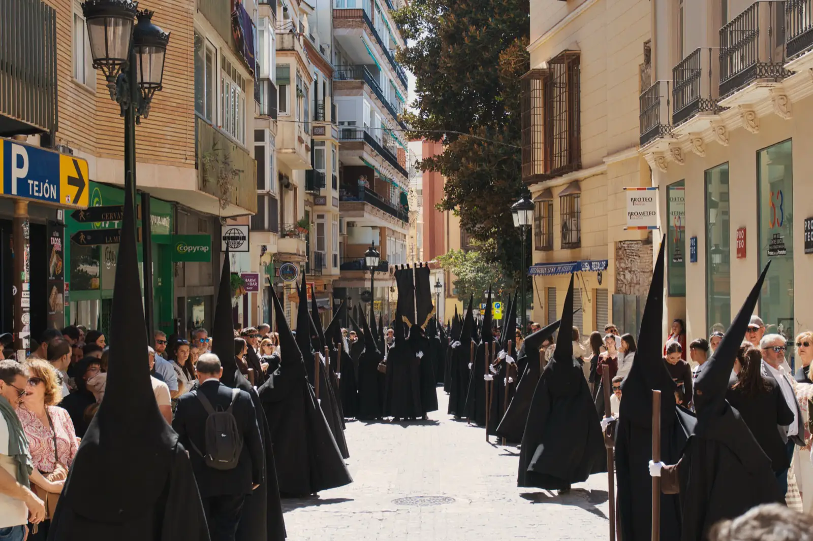 Nazareno penitent in black robes and hood during Semana Santa procession in Málaga
