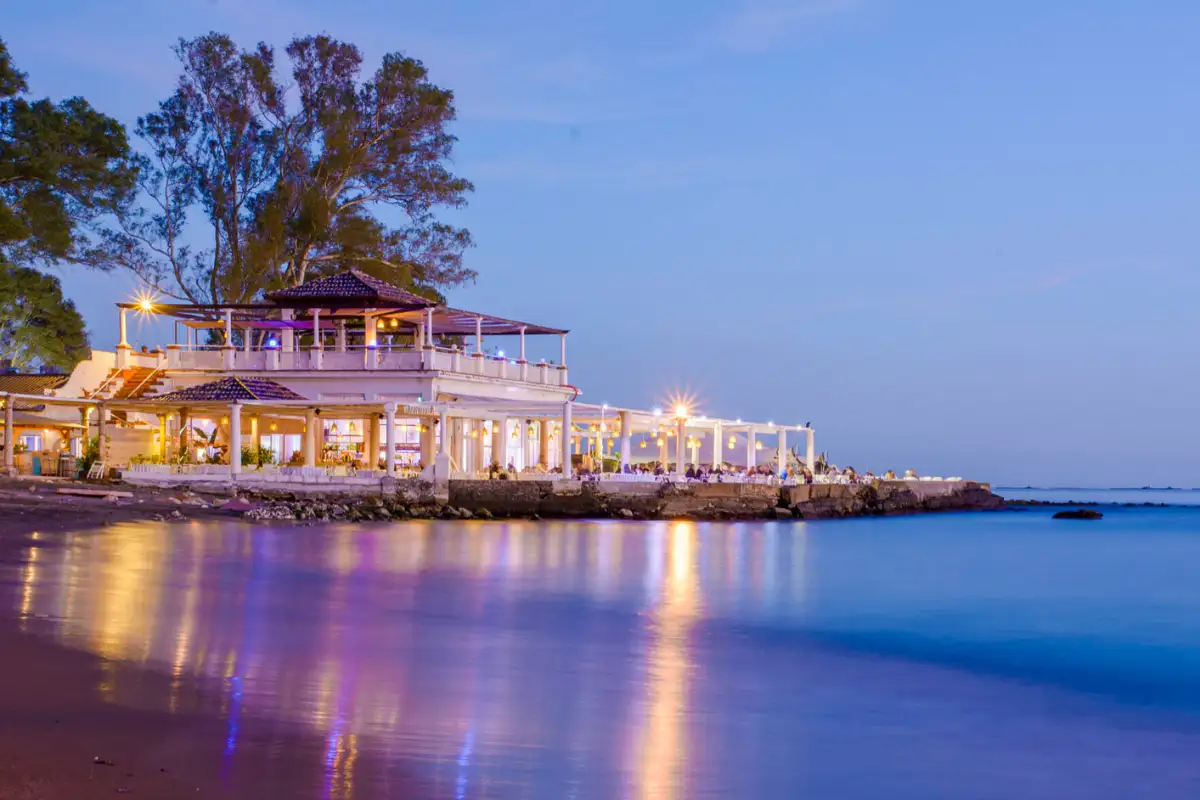 El Balneario's white pavilion on the rocks at Baños del Carmen at dusk, its lights reflected in the water