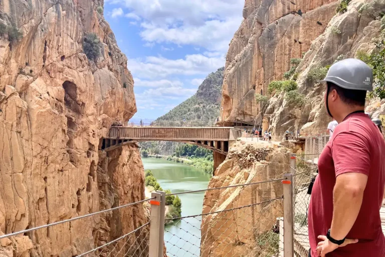 Hiker with a helmet looking across the Caminito del Rey gorge and suspension bridge near Málaga