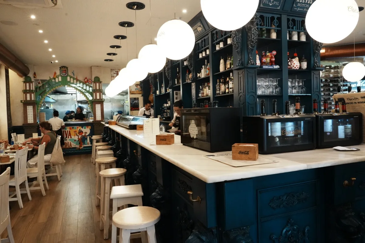 Inside Casa Lola, white stools along a blue carved bar under a row of globe lights, tables set to the left