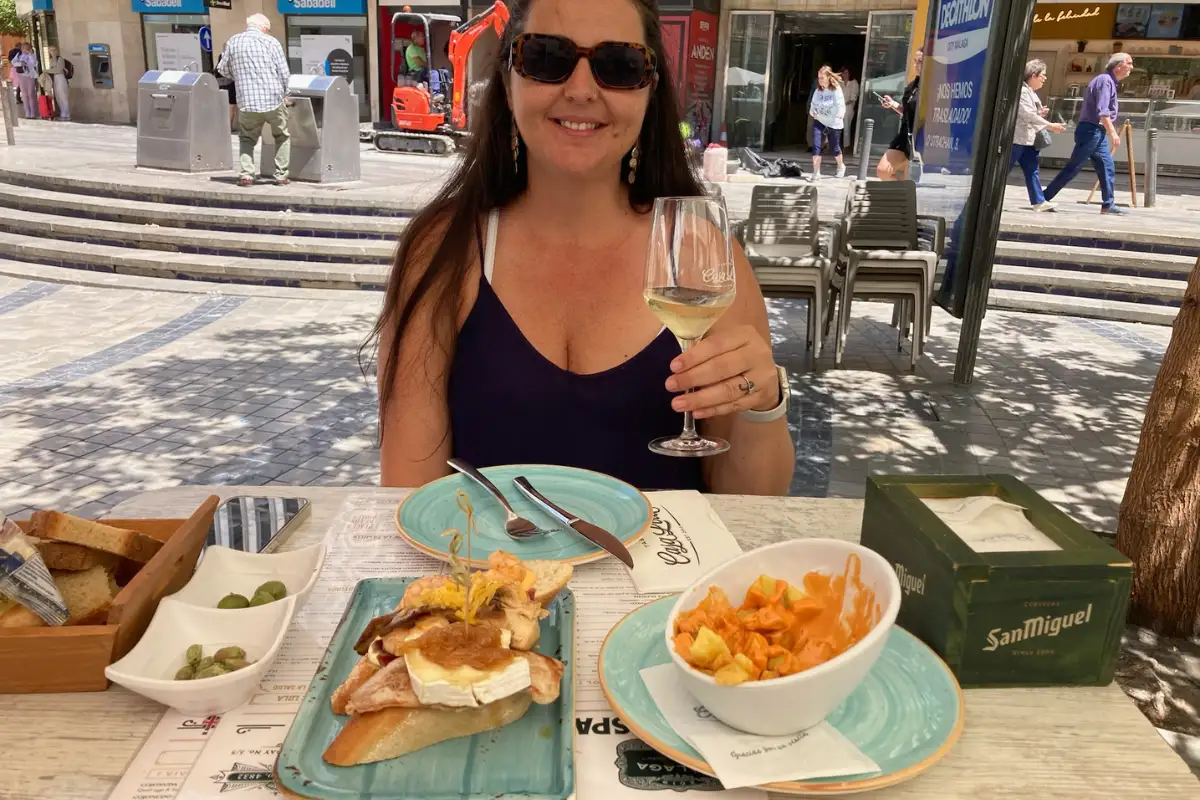 Woman enjoying tapas and white wine at an outdoor table at Casa Lola in Málaga
