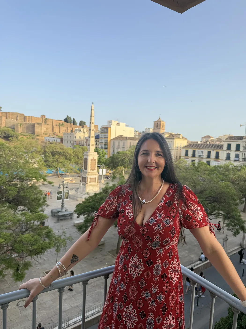 Heidi smiling on a balcony over Plaza de la Merced, with the Alcazaba visible in the background