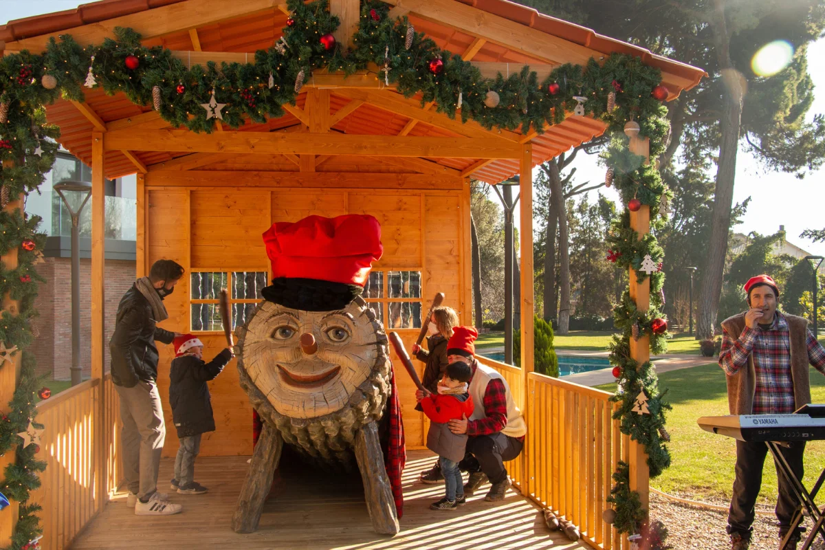 Three children are hitting a log with a smiling face called Caga Tio, hoping that sweets will fall out.